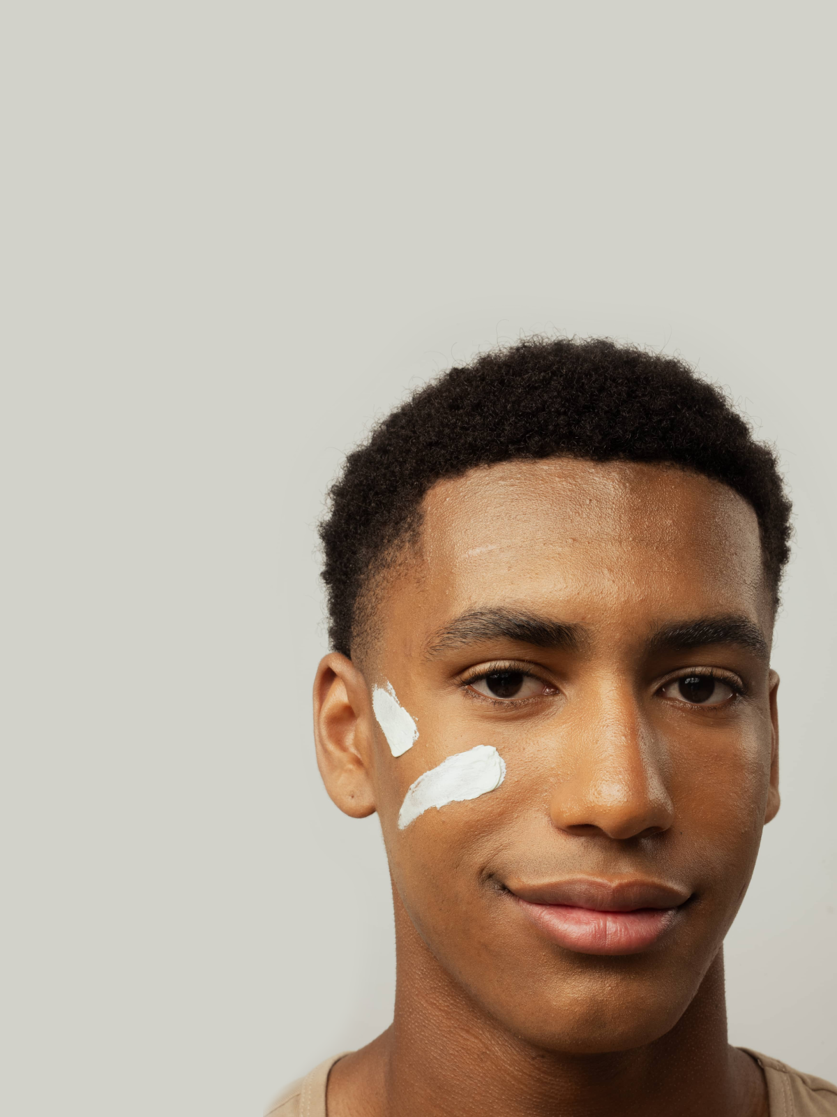 Portrait d’un jeune homme avec deux touches de crème appliquées sur la joue, sur fond neutre.