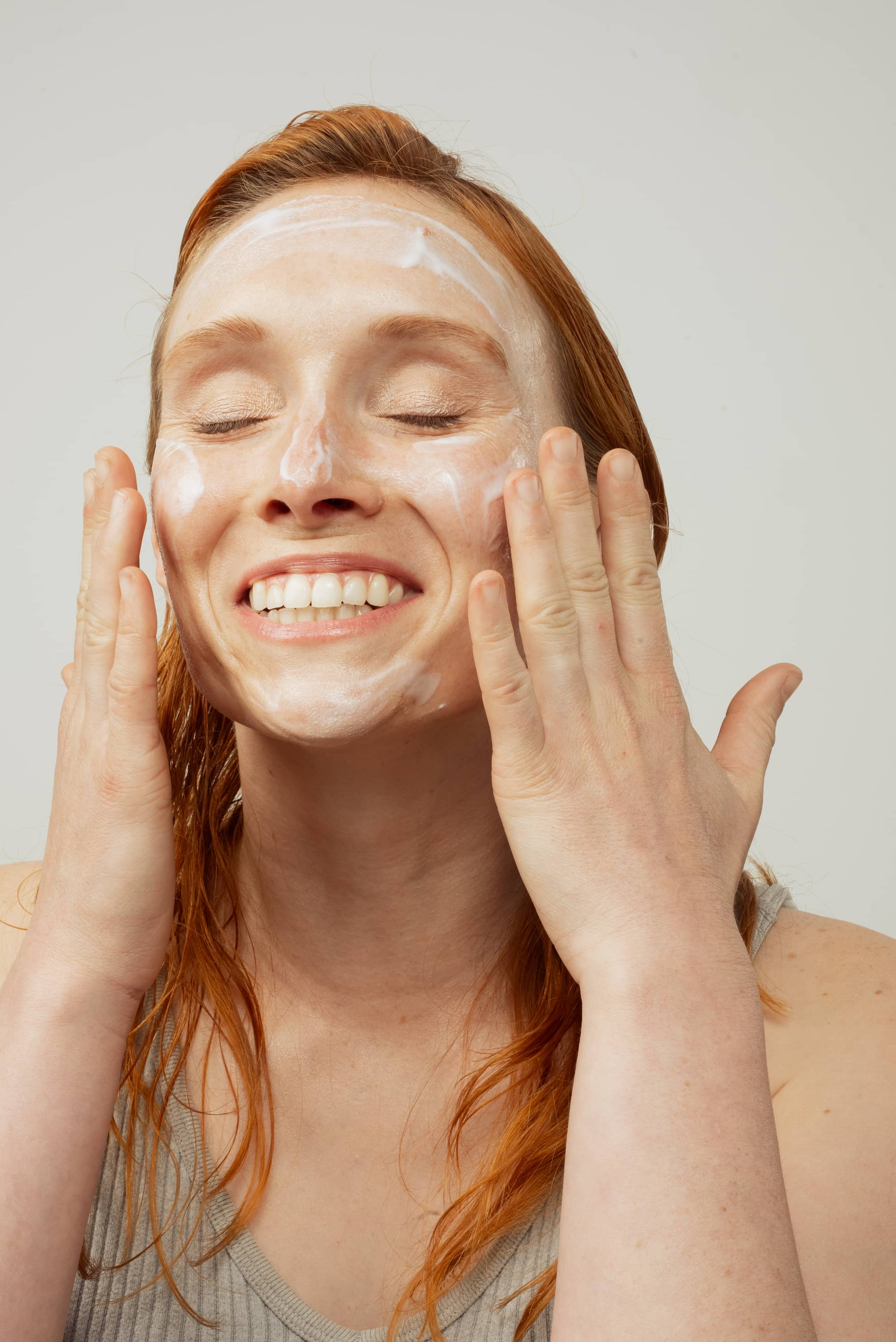 Femme appliquant un peeling effervescent, les yeux fermés et les mains posées sur les joues.